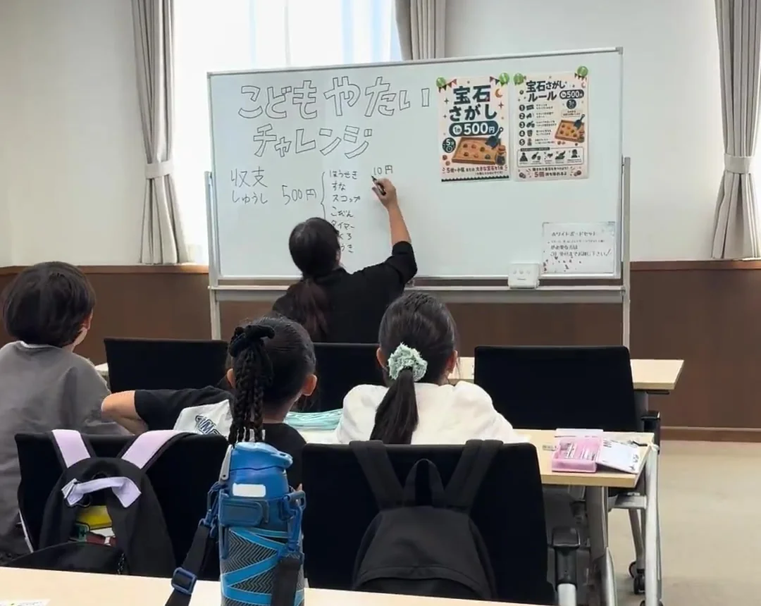 第3回の活動でホワイトボードを使ってお金の計算をしている様子。人物は後ろ姿のみで、顔は写っていません